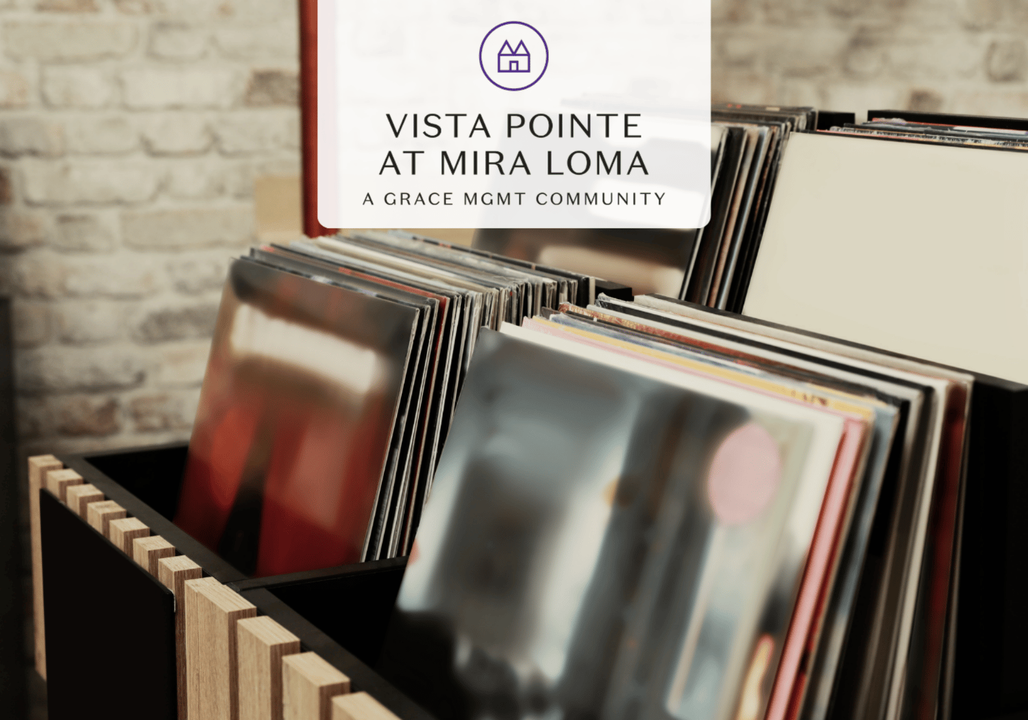 Vinyl records in a wooden rack with a translucent sign reading 'Vista Pointe at Mira Loma, A Grace Mgmt Community'