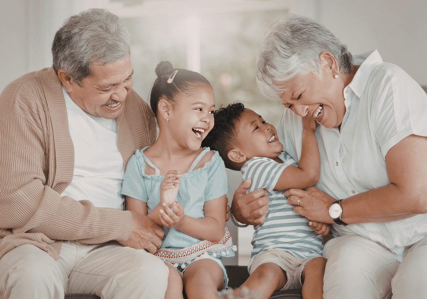 Grandfather and grandmother laughing with two young children on a couch.